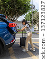 A teenager is standing next to a blue car and pulling a suitcase out of the trunk 137123827