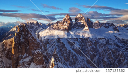 Panoramic winter view of the Dolomites at sunset with dramatic rocky peaks and snow covered ridges under colorful clouds, showcasing majestic alpine scenery in high resolution. 137123862