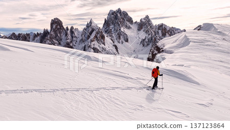 Ski mountaineer crossing a snowy ridge in the Dolomites with dramatic alpine peaks and blue sky in the background, capturing winter adventure and breathtaking mountain landscape. 137123864