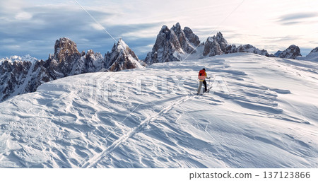 Ski mountaineer crossing a snowy ridge in the Dolomites with dramatic alpine peaks and blue sky in the background, capturing winter adventure and breathtaking mountain landscape. Ski mountaineer crossing a snowy ridge in the Dolomites with dramatic alpine peaks and blue sky in the background, capturing winter adventure and breathtaking mountain landscape. 137123866