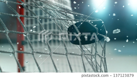 Action sports photo of a hockey puck flying into the goal net during a scoring shot, with ice particles in the air, capturing speed and intensity. 137123879