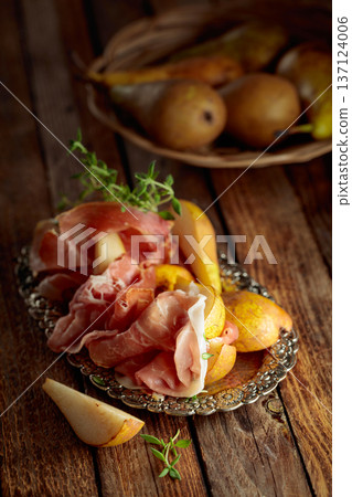 Prosciutto with pears and thyme on a silver tray. 137124006