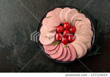 Various boiled sausages with tomatoes and rosemary on a stone table. 137124034