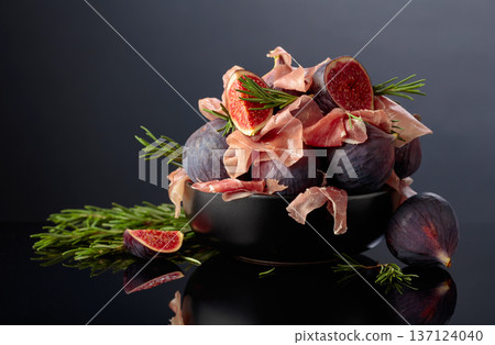 Prosciutto with rosemary and fig fruit on a black reflective background. Prosciutto with rosemary and fig fruit on a black reflective background. 137124040