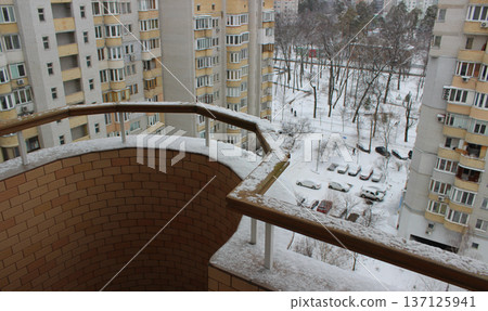 View from a snow-covered balcony of cars under snow parked near multi-storey buildings 137125941