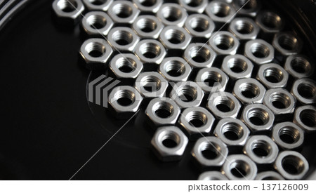 Iron nuts on a black flat surface are huddled together on the right side of the image 137126009