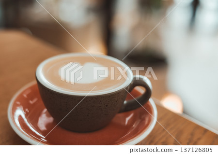 Close-up of a cup of hot latte art with a heart shape on a wooden table in a cafe. Coffee shop, morning routine, and lifestyle design themes. Close-up of a cup of hot latte art with a heart shape on a wooden table in a cafe. Coffee shop, morning routine, and lifestyle design themes. 137126805