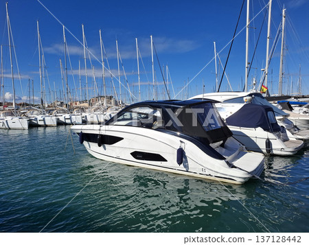 A modern motorboat is moored in a turquoise harbor with other boats nearby. The sky is clear and blue, showing a nice summer day. The boat looks sleek and new. A modern motorboat is moored in a turquoise harbor with other boats nearby. The sky is clear and blue, showing a nice summer day. The boat looks sleek and new. 137128442