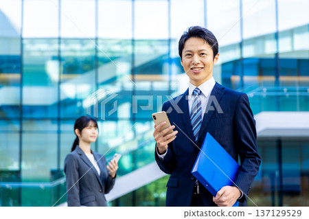 Young businessman, skyscraper, smartphone, business image Young businessman, skyscraper, smartphone, business image 137129529