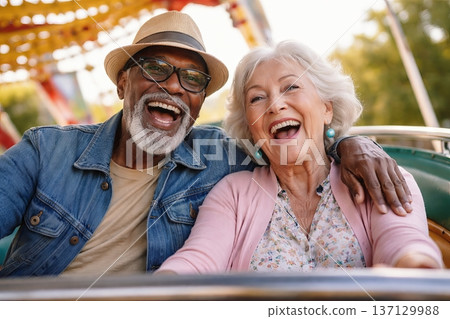 Senior african american man and caucasian woman joyfully riding a roller coaster at an amusement park on a sunny day. concept of adventure, happiness, and enjoying life. 137129988