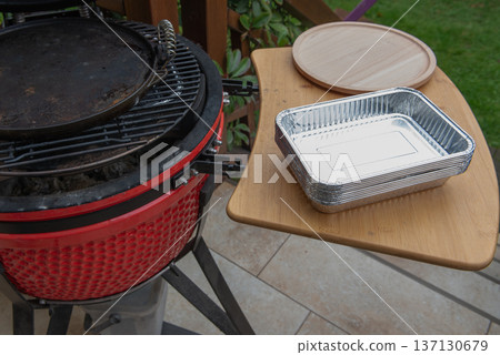 Ceramic grill with disposable aluminum trays on side shelf outdoors Ceramic grill with disposable aluminum trays on side shelf outdoors 137130679