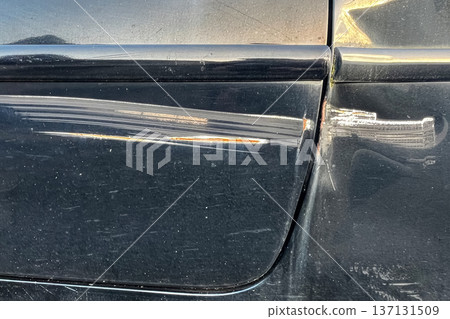 Scratched black car door with rust marks and damaged paint surface close up showing vehicle body detail and wear. Scratched black car door with rust marks and damaged paint surface close up showing vehicle body detail and wear. 137131509