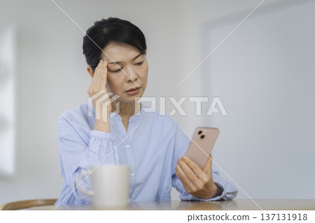A woman in her late 50s pondering while looking at her smartphone 137131918
