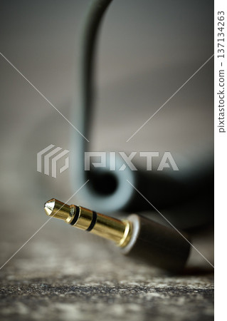 Macro shot of a gold-plated stereo mini-plug connector with a blurred cable on a textured surface Macro shot of a gold-plated stereo mini-plug connector with a blurred cable on a textured surface 137134263