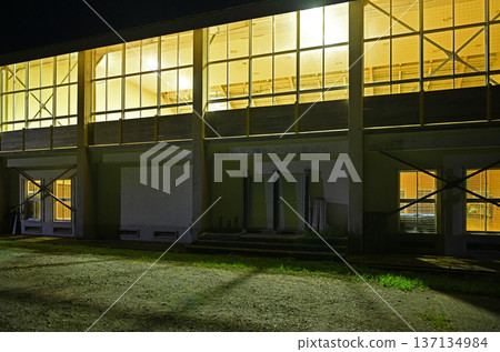 An abandoned school gymnasium in Satoyama, with windows lit up in the darkness of the night 137134984