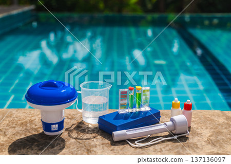 Liquid pool chemicals poured into swimming pool water using a transparent measuring cup with volume markings 137136097