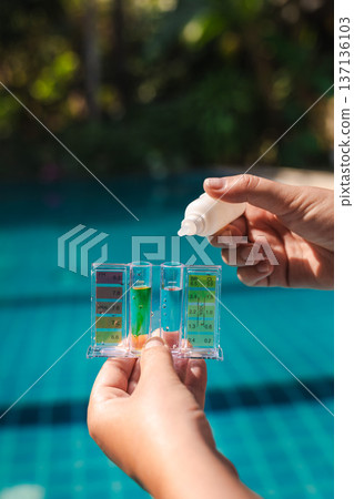 Hand holding pool water test kit measuring pH level and chlorine concentration in swimming pool during routine maintenance and water quality control Hand holding pool water test kit measuring pH level and chlorine concentration in swimming pool during routine maintenance and water quality control 137136103
