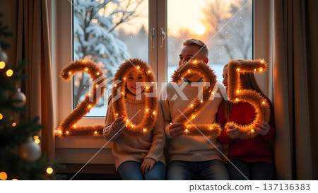 In a cozy room, the family poses by a big window showcasing a snowy view. Each member holds part of a luminous 2025 garland, celebrating the festive season 137136383