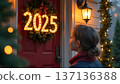 Under a winter sun, the family decorates their front door with wreaths and garlands. 2025 crafted from Christmas lights hangs brightly, while parents and kids share smiles 137136388