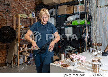Teacher prepares for crochet master class. Woman laying out threads hooks and samples of products on table. 137136503