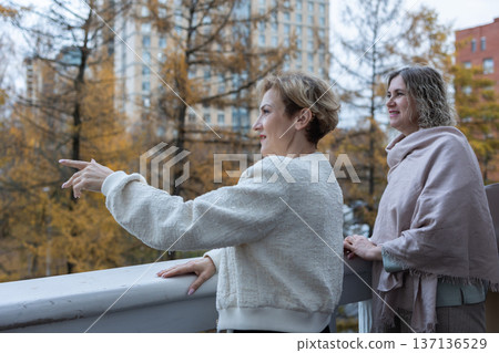 Communication. Female friends meeting outdoors on terrace gesturing hands and sharing conversation in cool season city environment. Communication. Female friends meeting outdoors on terrace gesturing hands and sharing conversation in cool season city environment. 137136529