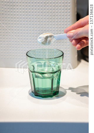 Woman's hand pours white collagen powder with spoon into transparent glass of water. High quality photo Woman's hand pours white collagen powder with spoon into transparent glass of water. High quality photo 137136628