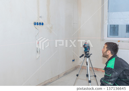 Man makes repairs in new apartment. Builder levels walls using laser level. High quality photo Man makes repairs in new apartment. Builder levels walls using laser level. High quality photo 137136645