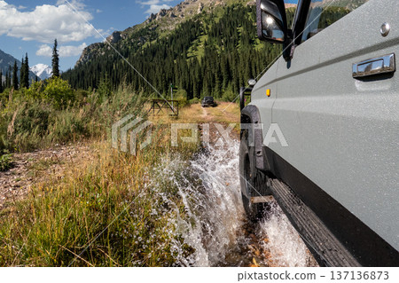 Close-up of an off-road vehicle wheel splashing water while driving on a mountain road. Close-up of an off-road vehicle wheel splashing water while driving on a mountain road. 137136873