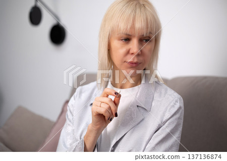 Woman taking tablets while resting on sofa emphasizing sickness treatment medication use and personal wellbeing indoors. Woman taking tablets while resting on sofa emphasizing sickness treatment medication use and personal wellbeing indoors. 137136874