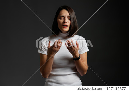Young woman looking devastated and emotional with her hands raised in a gesture of despair or prayer. Young woman looking devastated and emotional with her hands raised in a gesture of despair or prayer. 137136877