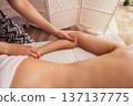 Therapist gently massages a woman arm and elbow on a white massage table, soft warm light highlighting smooth skin and creating a calm, restorative spa wellness atmosphere. 137137775