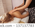 Spa therapist gives a relaxing back massage to a blonde woman lying face down on a white towel warm soft light and neutral tones create a calm, intimate wellness moment 137137783
