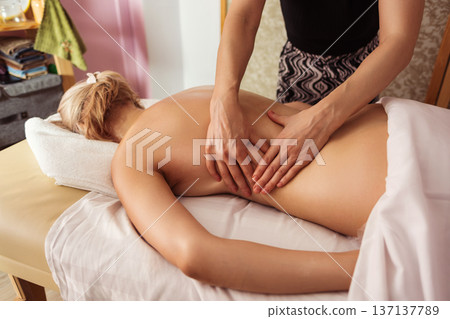 Close-up view of professional massage therapist performing back massage on a blonde woman lying on table, in spa room with warm light, calm tones, and relaxing atmosphere. Close-up view of professional massage therapist performing back massage on a blonde woman lying on table, in spa room with warm light, calm tones, and relaxing atmosphere. 137137789