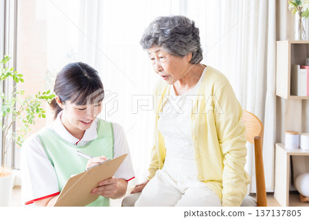 一位老年婦女在家中接受上門護理師的醫療問診。 137137805