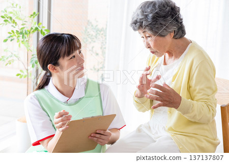 Senior woman undergoing a medical interview at home with a visiting nurse 137137807
