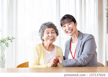 一位微笑的老婦人和幾位女工作人員正在照顧老人。 137137820