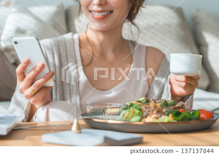 A woman looking at her smartphone while eating breakfast or lunch (app, SNS) 137137844