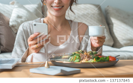 A woman looking at her smartphone while eating breakfast or lunch (app, SNS) 137137845