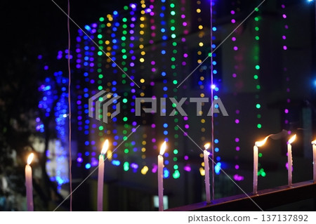 Burning candles on railing with colorful bokeh festive lights background Burning candles on railing with colorful bokeh festive lights background 137137892