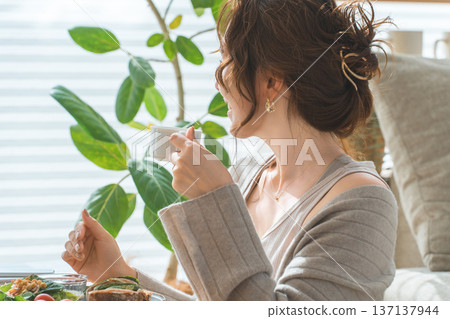 Stylish young Asian woman eating at the living room table Stylish young Asian woman eating at the living room table 137137944