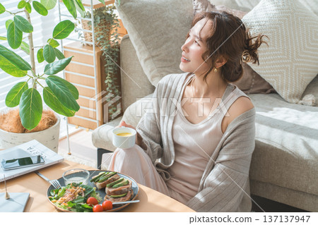 一位時尚的年輕亞裔女性正在客廳餐桌旁用餐。 一位時尚的年輕亞裔女性正在客廳餐桌旁用餐。 137137947