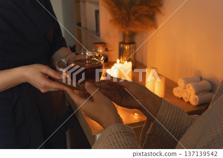 Hands giving cup tea with warm candlelight. Person receiving hot cup of tea from another, relaxing in cozy, intimate atmosphere with glowing candles Hands giving cup tea with warm candlelight. Person receiving hot cup of tea from another, relaxing in cozy, intimate atmosphere with glowing candles 137139542