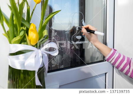 Creative enthusiastic unrecognizable woman paint window with white marker. Easter bunny rabbit decoration on big clear window. Springtime idea home decoration 137139735
