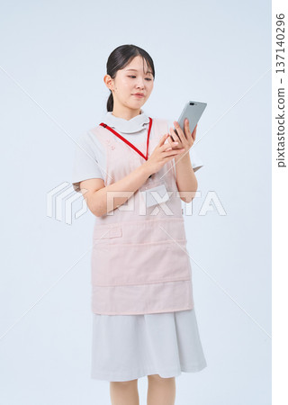 A young woman wearing a white coat and apron and holding a digital device A young woman wearing a white coat and apron and holding a digital device 137140296