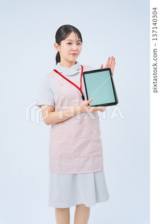 一位身穿白大褂和圍裙、手持電子設備的年輕女子 一位身穿白大褂和圍裙、手持電子設備的年輕女子 137140304
