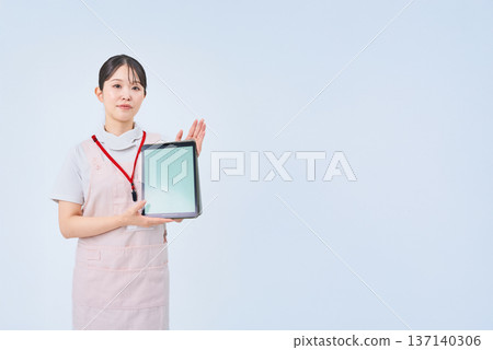 A young woman wearing a white coat and apron and holding a digital device 137140306
