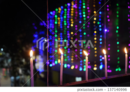 Row of lit candles on balcony railing against vibrant multicolored bokeh background Row of lit candles on balcony railing against vibrant multicolored bokeh background 137140996