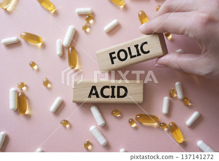 Folic acid symbol. Wooden blocks with words Folic acid. Beautiful pink background with pills. Doctor hand. Medicine and Folic acid concept. Copy space. Folic acid symbol. Wooden blocks with words Folic acid. Beautiful pink background with pills. Doctor hand. Medicine and Folic acid concept. Copy space. 137141272