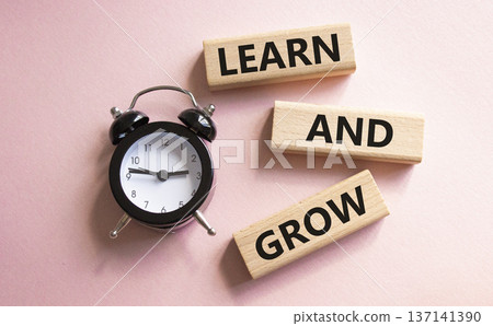 Learn and grow symbol. Concept words Learn and grow on wooden blocks. Beautiful pink background with alarm clock. Business and Learn and grow concept. Copy space. 137141390