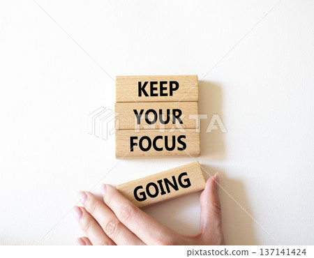 Focus symbol. Concept words Keep Your Focus Going on wooden blocks. Beautiful bright white background. Businessman hand. Business and Keep Your Focus Going concept. Copy space. 137141424